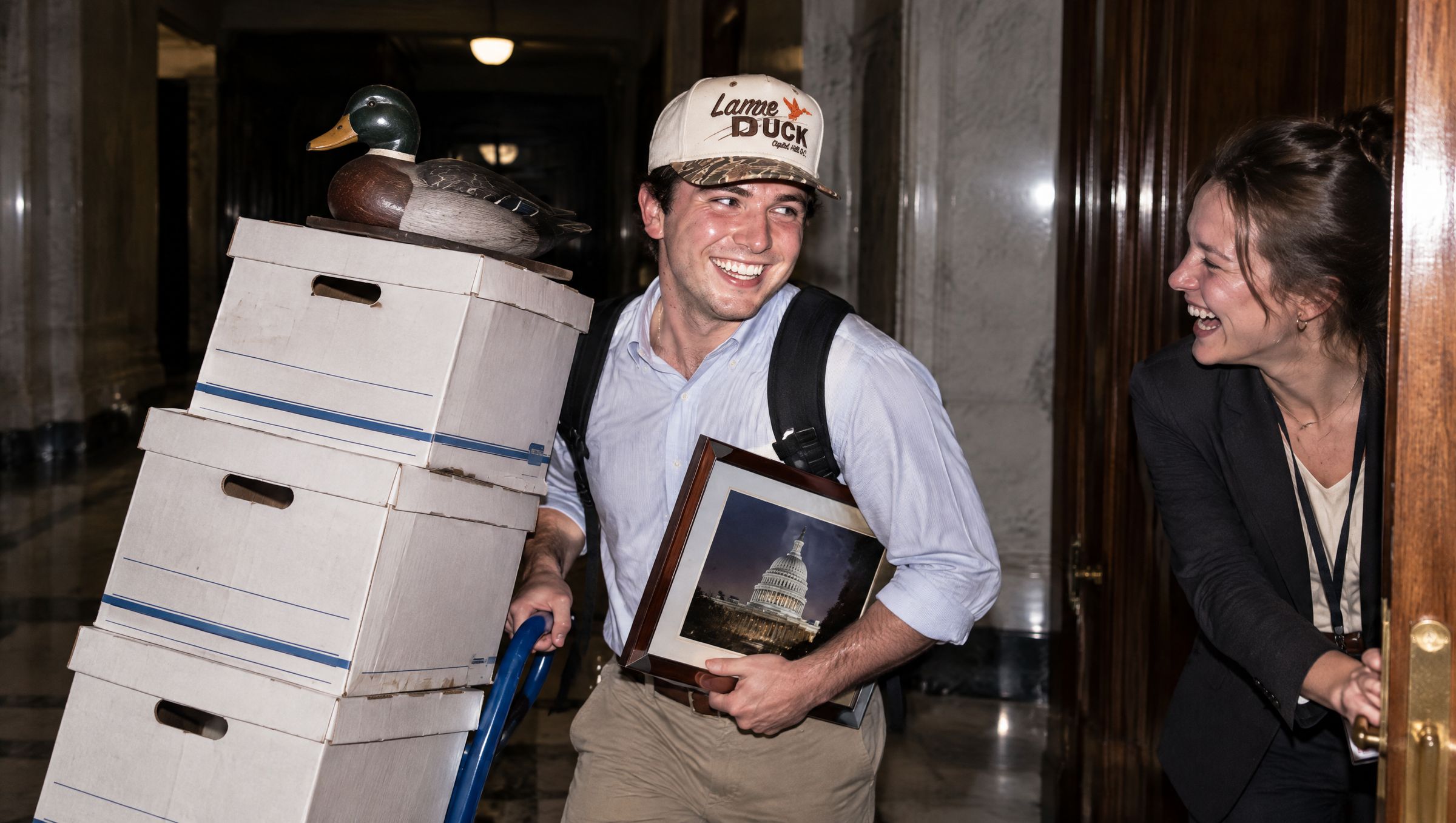 A staffer wheeling a tower of file boxes topped with a mallard decoy down a marble hallway in the Lame Duck cap while a colleague laughs in the doorway