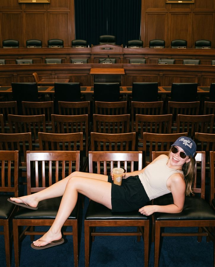 A staffer lounging across hearing room chairs in the navy August Recess cap