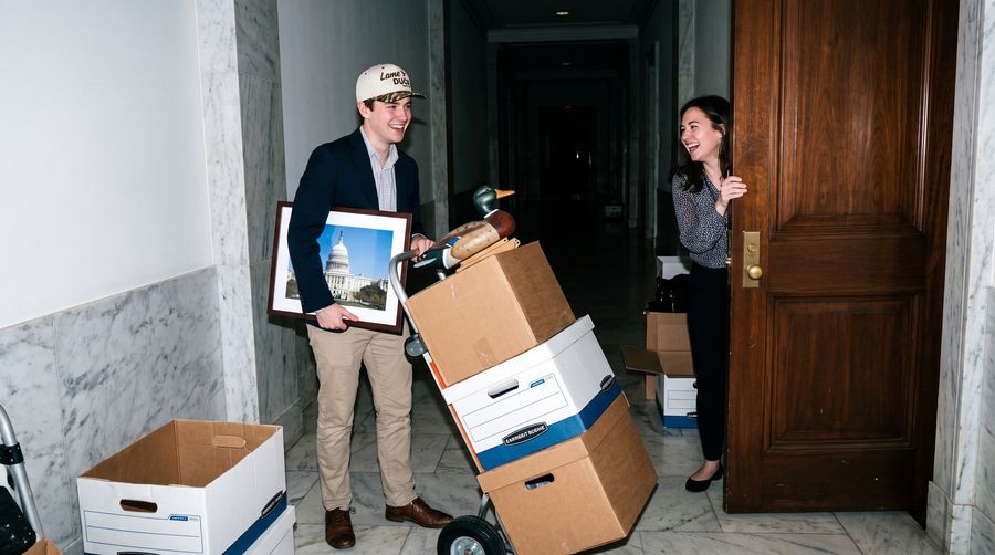 A staffer wheeling a hand truck of boxes topped with a duck decoy down a marble hallway in the Lame Duck cap